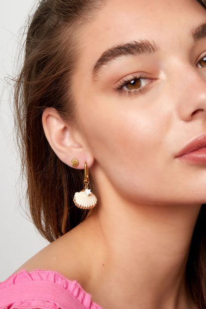 Woman wearing small gold shell stud earrings paired with dangling shell and star charm earrings