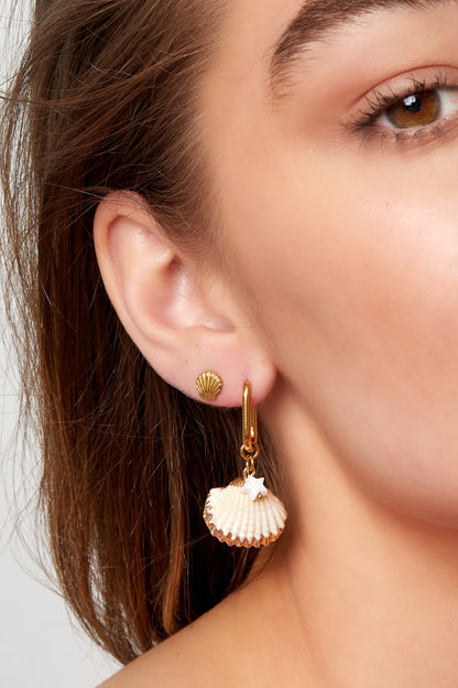 Close-up of woman wearing gold shell stud earrings paired with dangling shell and star charm earrings
