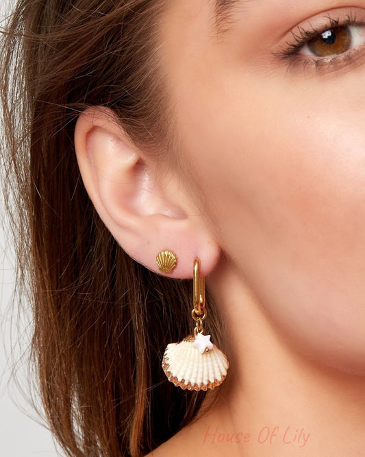 Close-up of woman wearing gold shell stud earrings paired with dangling shell and star charm earrings