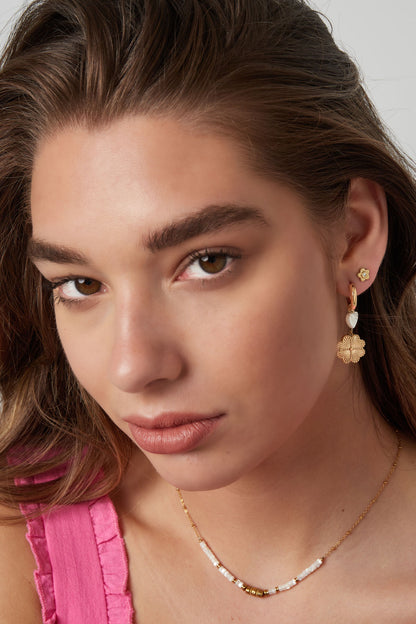 Model close-up showing youthful styling with gold flower stud earrings worn with a pink ruffled top and beaded necklace