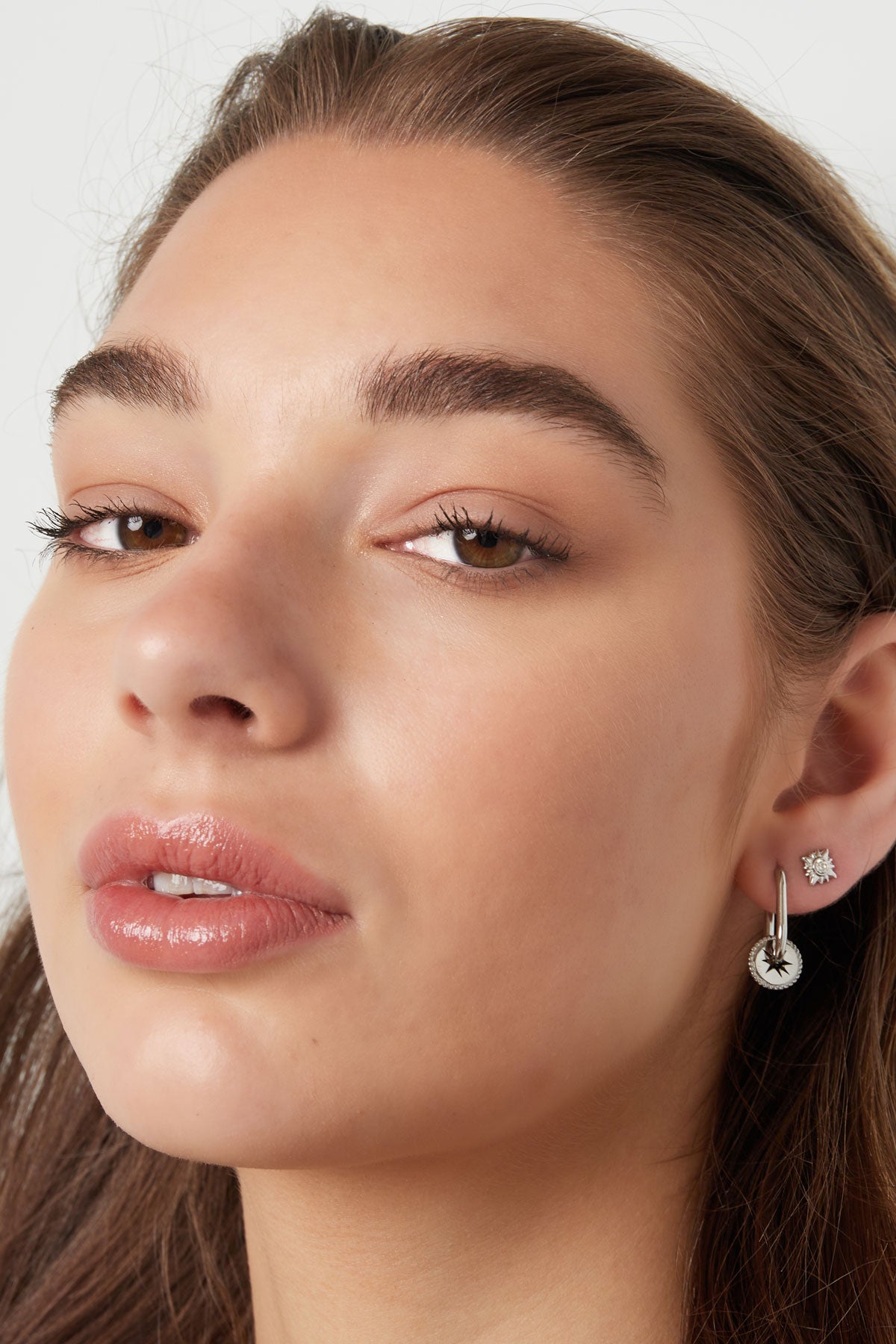 Portrait of woman wearing silver sunburst crystal stud earrings with neutral makeup and natural hair