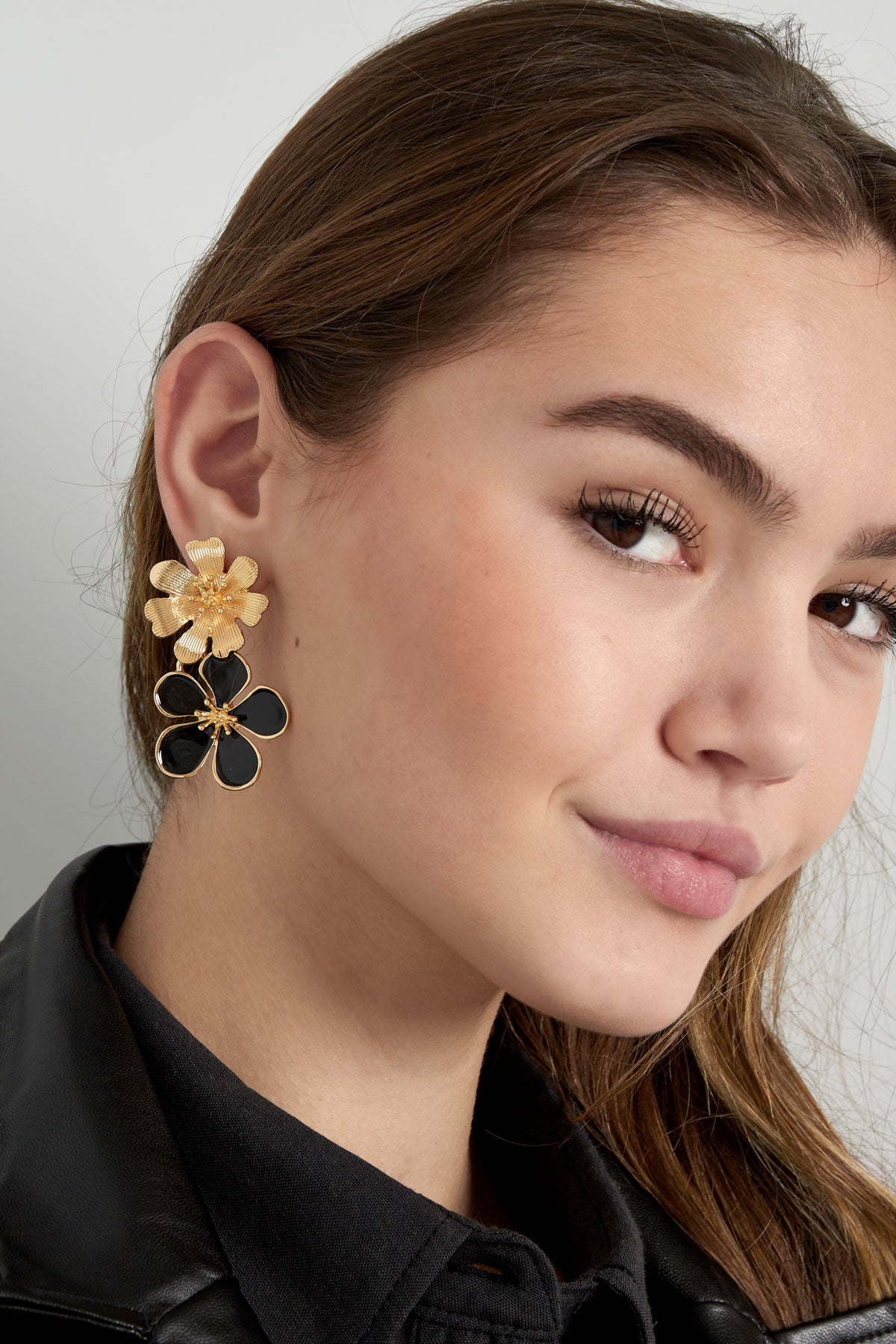 Pair of gold-tone drop earrings with textured top flower and white enamel bottom flower on white background