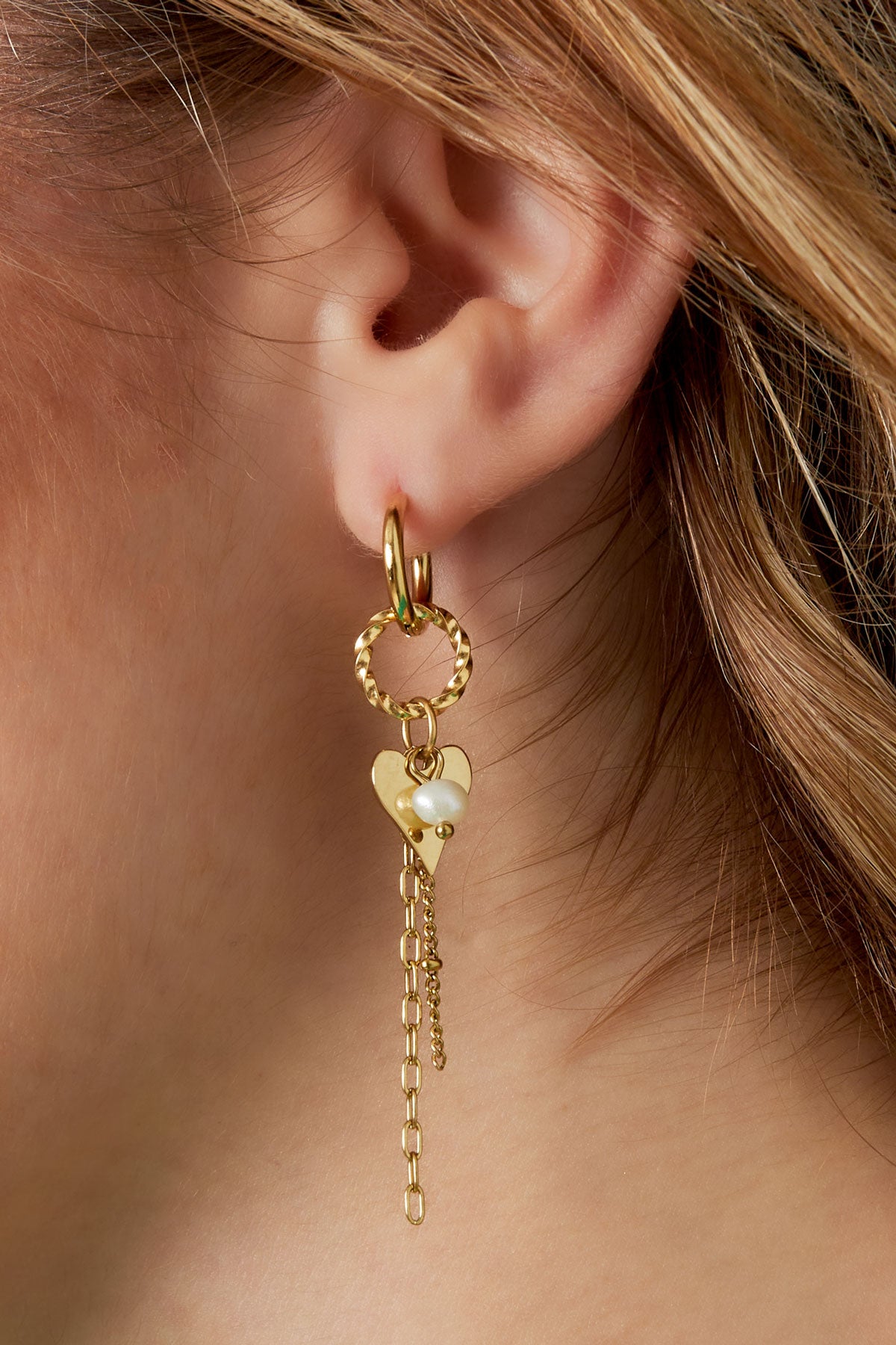 Close-up of woman's ear showing gold dangle hoops with heart charm and pearl accent dangling down
