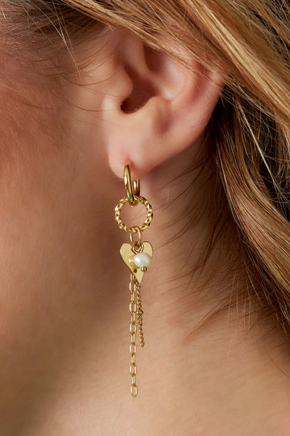 Close-up of woman's ear showing gold dangle hoops with heart charm and pearl accent dangling down