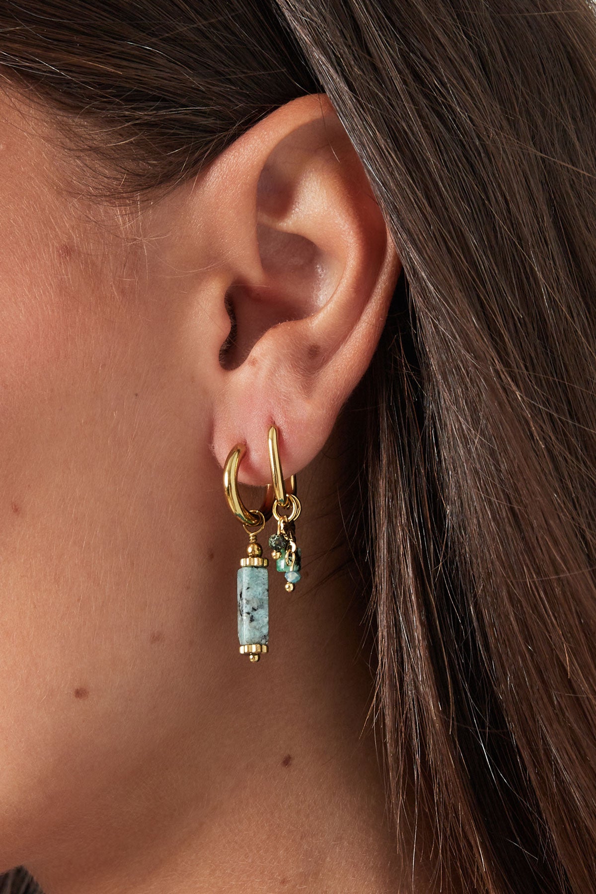 Close up of woman's ear adorned with gold hoop earrings featuring turquoise stone charms and small green beads