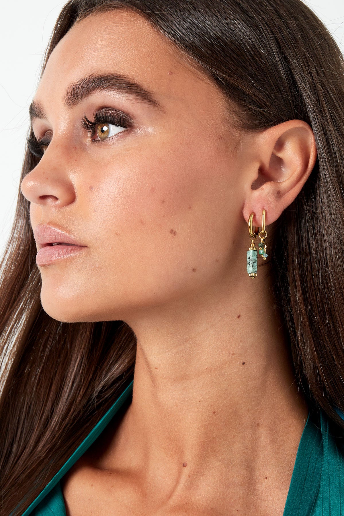 Side profile of woman wearing dark green top and gold hoop earrings with turquoise stone dangles