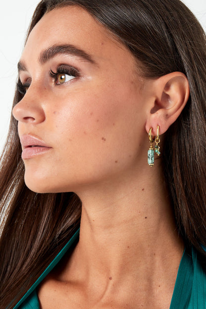 Side profile of woman wearing dark green top and gold hoop earrings with turquoise stone dangles