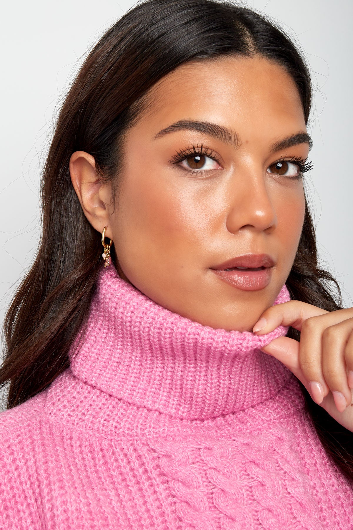 Woman wearing pink turtleneck sweater and gold hoop earrings with pink stone charms