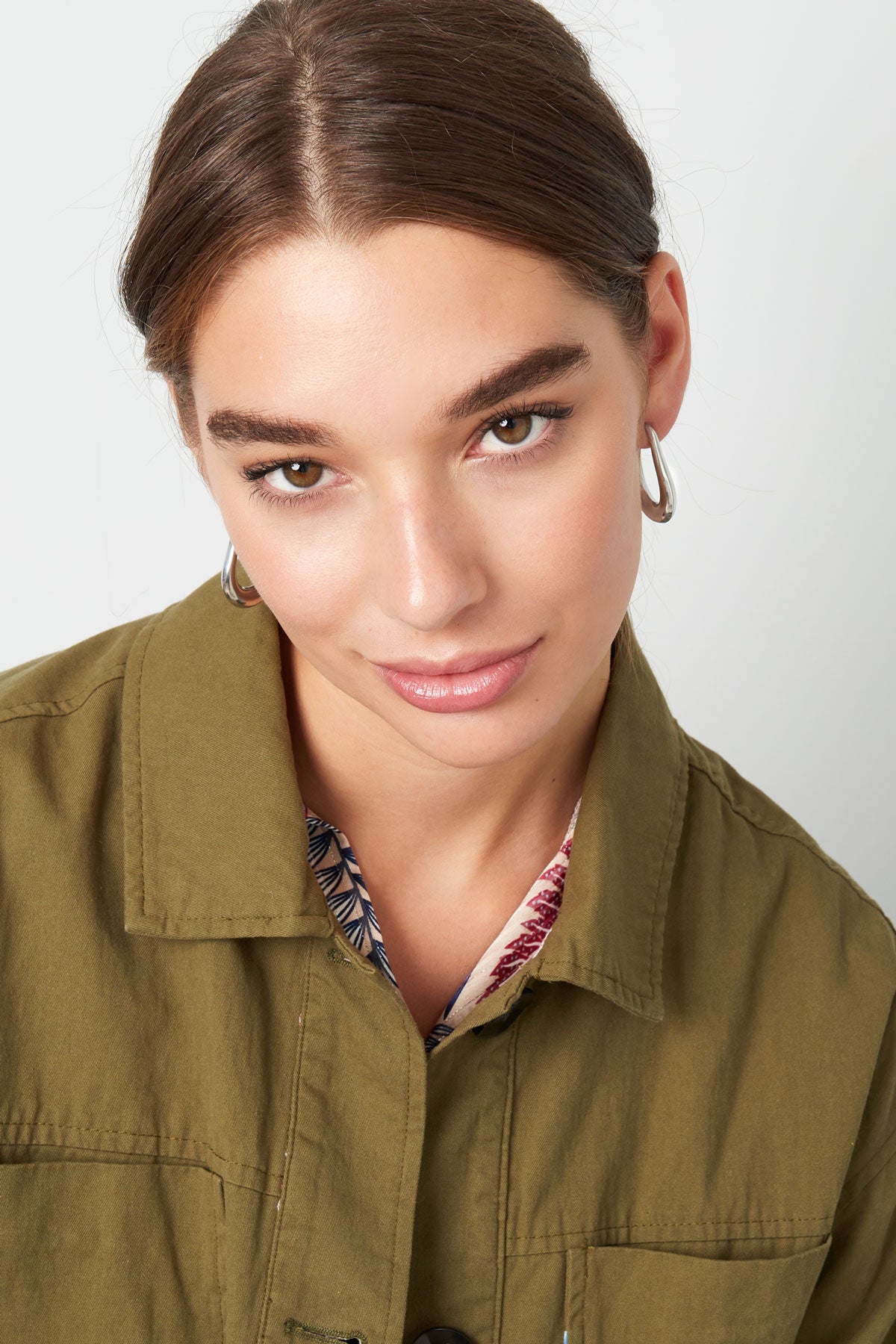 Model wearing silver teardrop hoop earrings, front-facing with playful gaze and olive green jacket