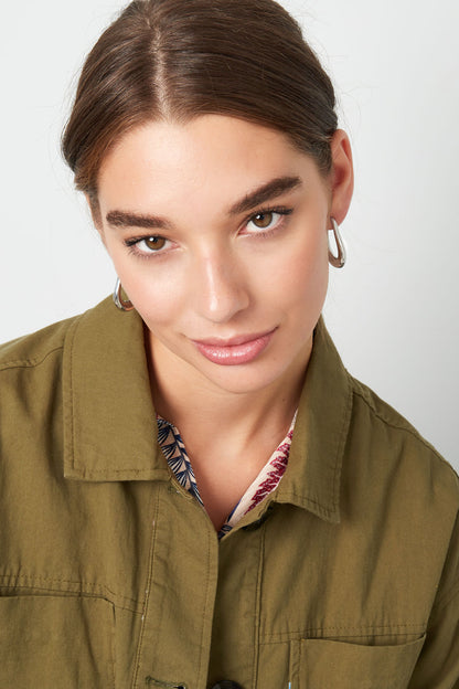 Model wearing silver teardrop hoop earrings, front-facing with playful gaze and olive green jacket