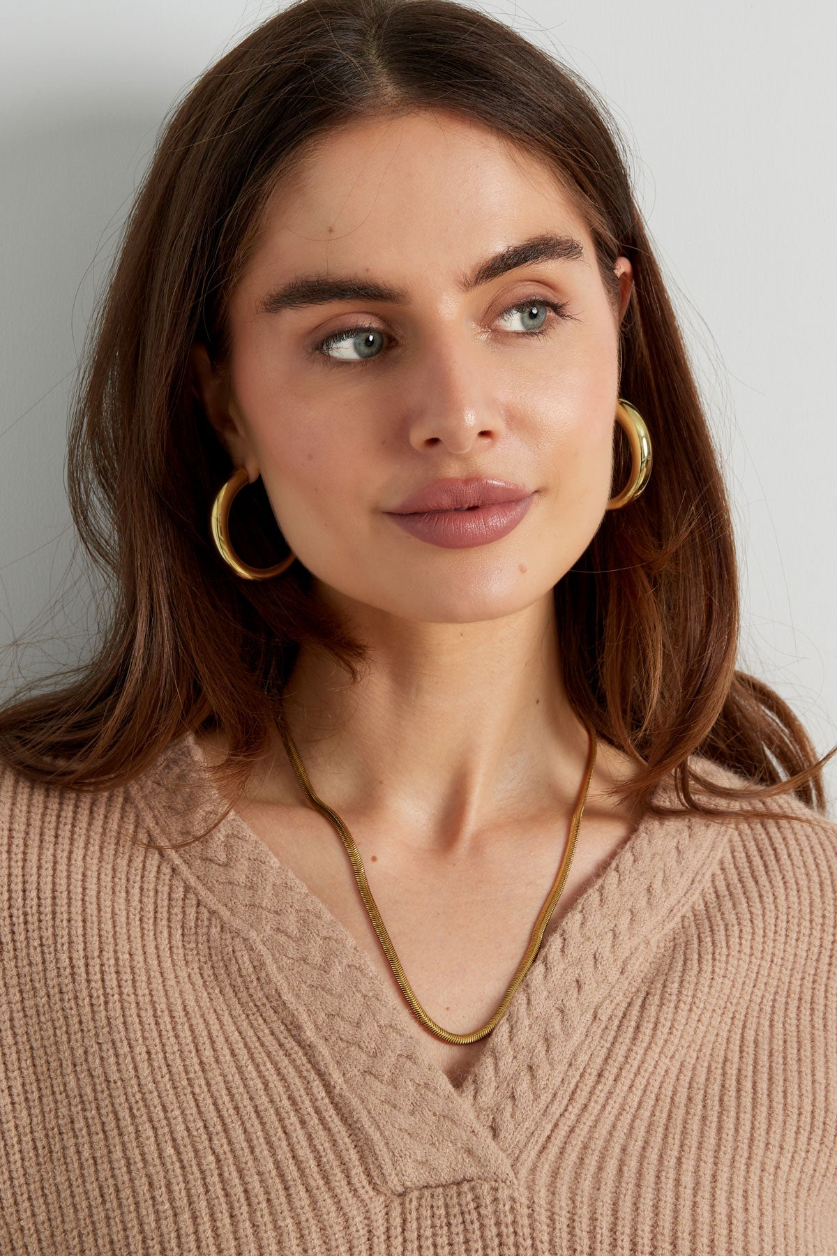 Young woman wearing chunky gold curved hoop earrings and beige knit top