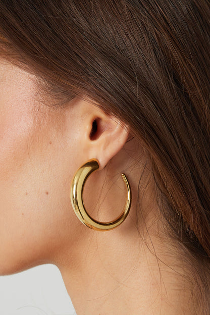 Close-up side profile of woman wearing chunky gold curved hoop earrings