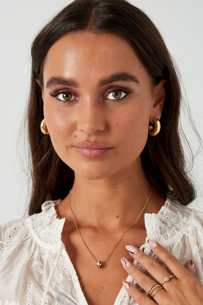 Close-up front view of woman wearing chunky gold hoop earrings and white textured blouse