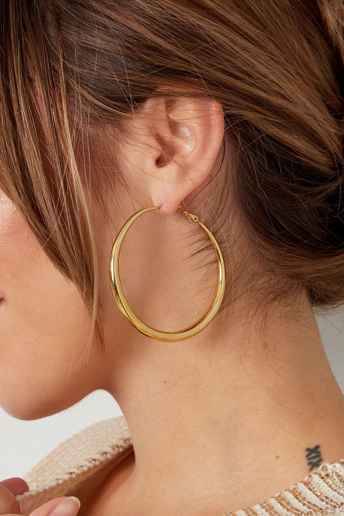 Side view of woman with light brown hair wearing large gold hoop earring and beige sweater