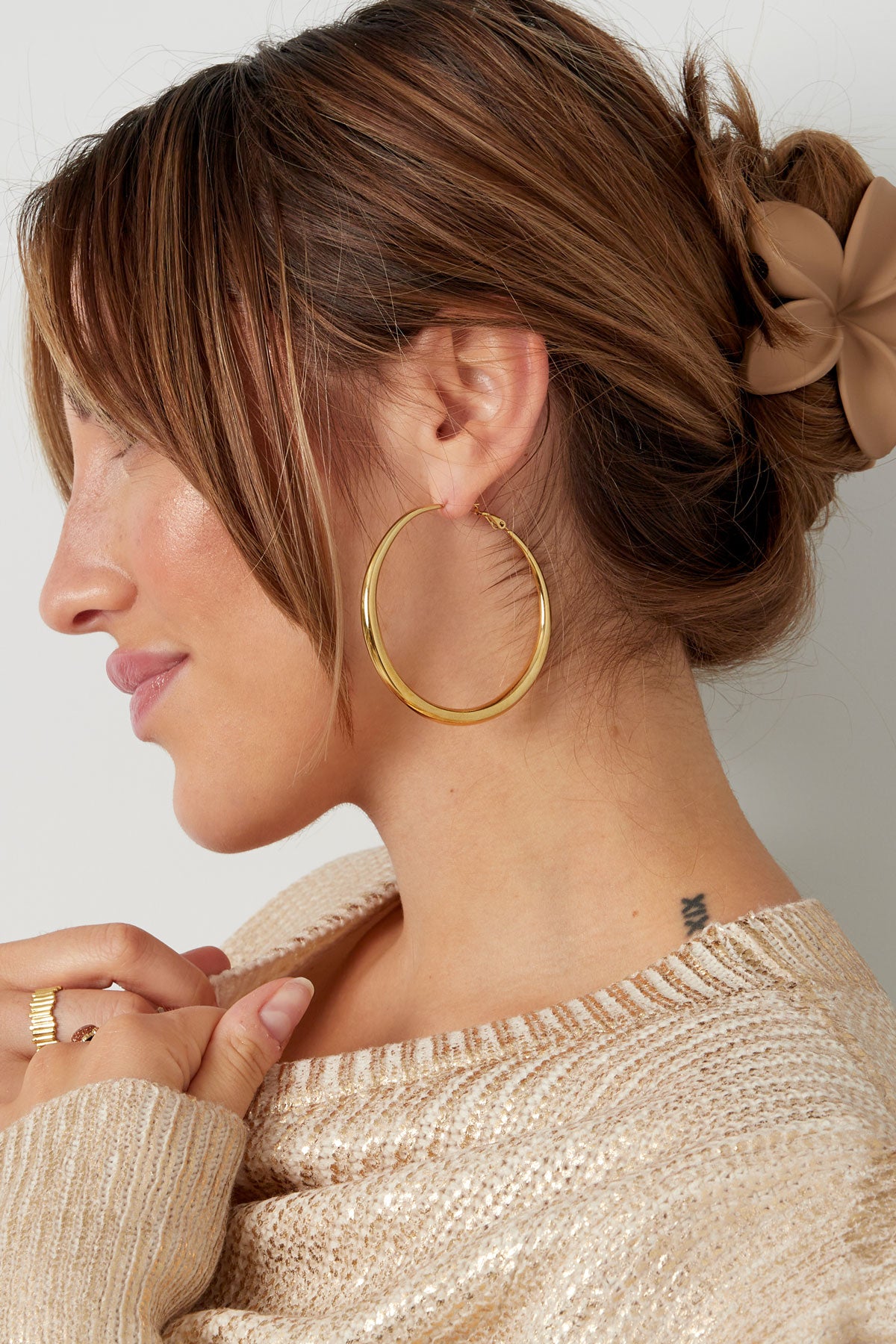 Profile of woman with dark hair in a bun wearing gold hoop earring and smiling