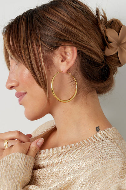 Profile of woman with dark hair in a bun wearing gold hoop earring and smiling