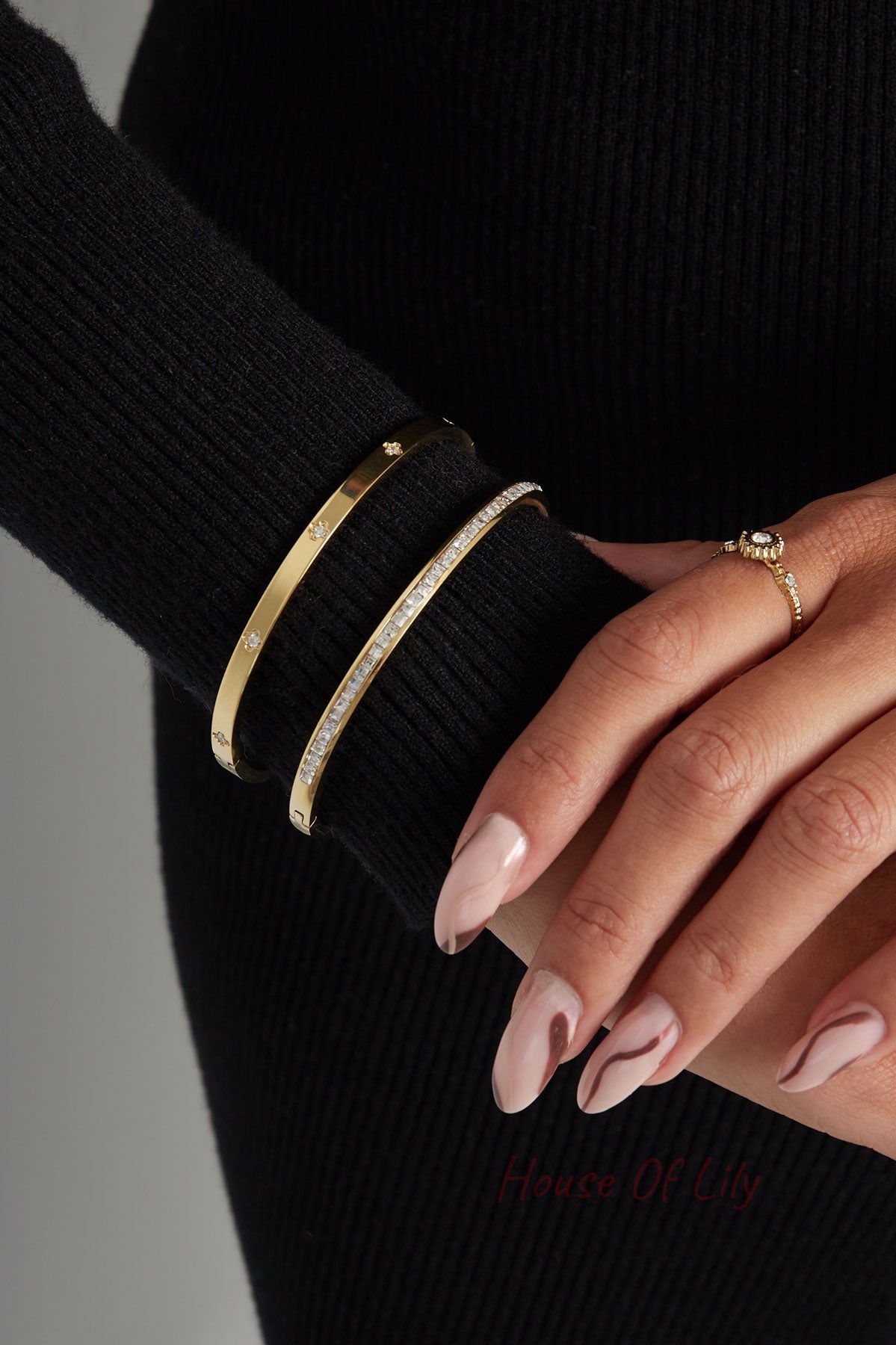 Close-up of woman's wrist wearing two gold-tone bangles, one with clear crystals, paired with a gold ring and black long sleeve