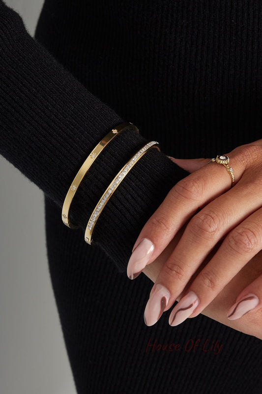 Close-up of woman's wrist wearing two gold-tone bangles, one with clear crystals, paired with a gold ring and black long sleeve