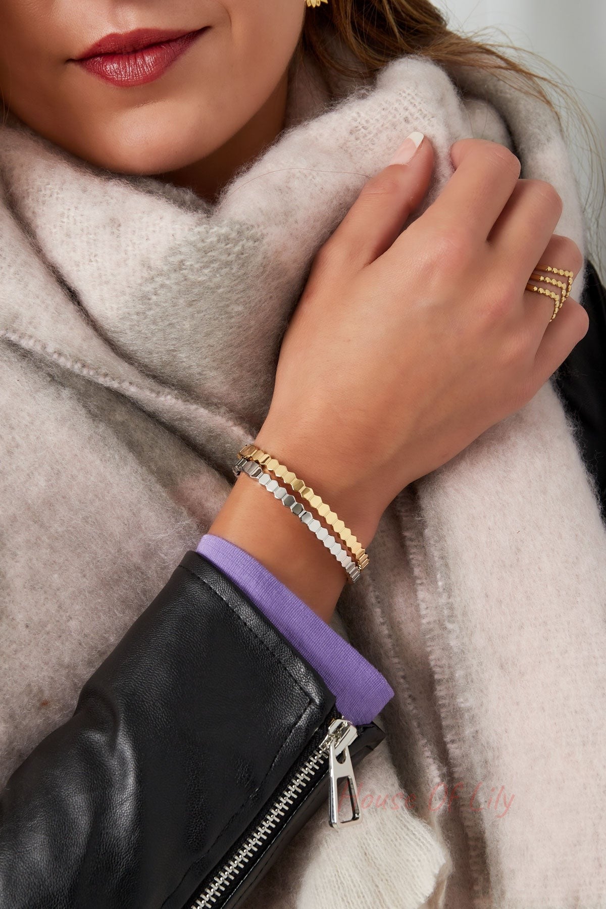 Close-up of woman's wrist with gold and silver hexagon link bracelets, beige scarf, and black jacket sleeve