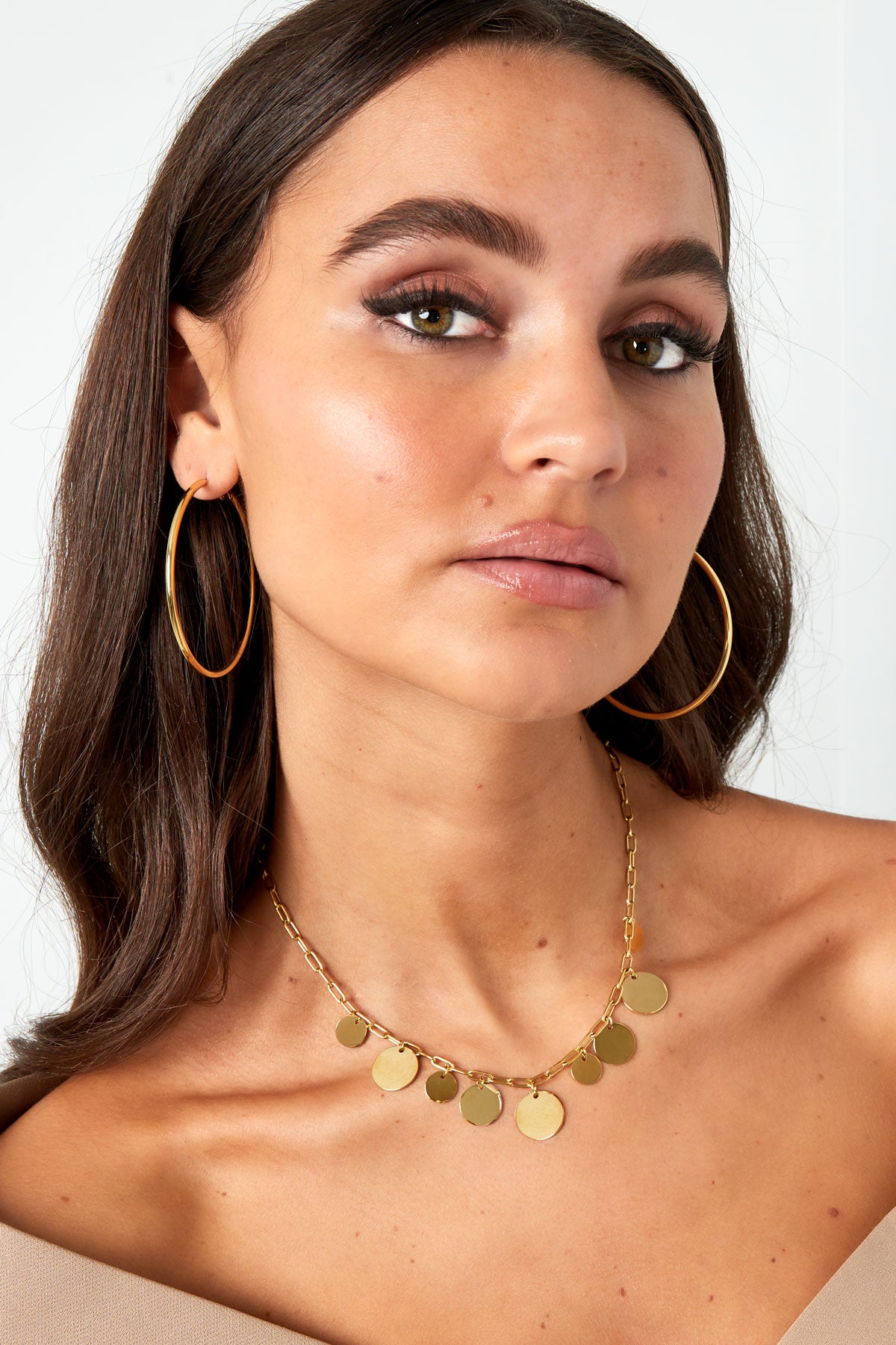 Woman wearing large gold hoop earrings and a gold coin charm necklace, showcasing youthful and minimal style