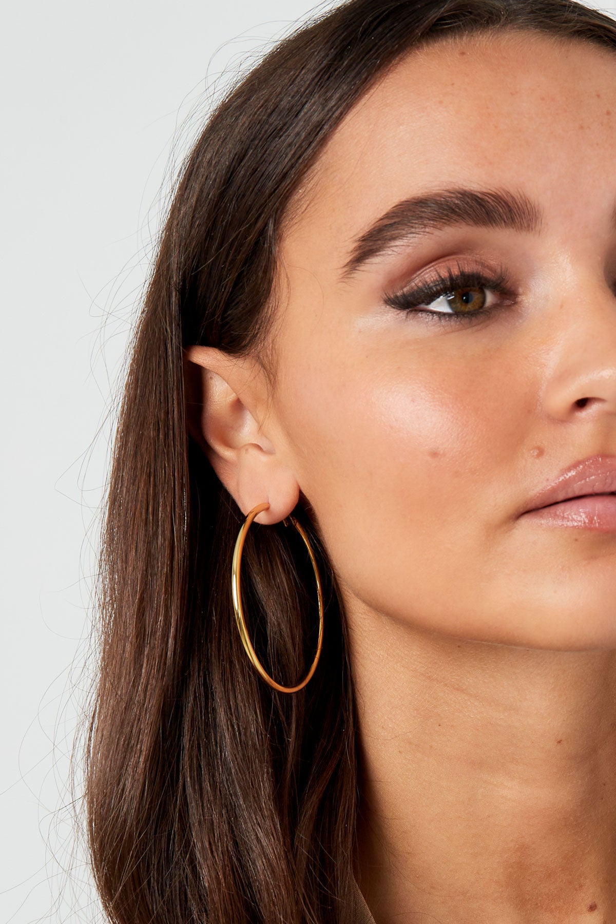 Close up side profile of a woman wearing smooth gold hoop earrings, highlighting simple and elegant design
