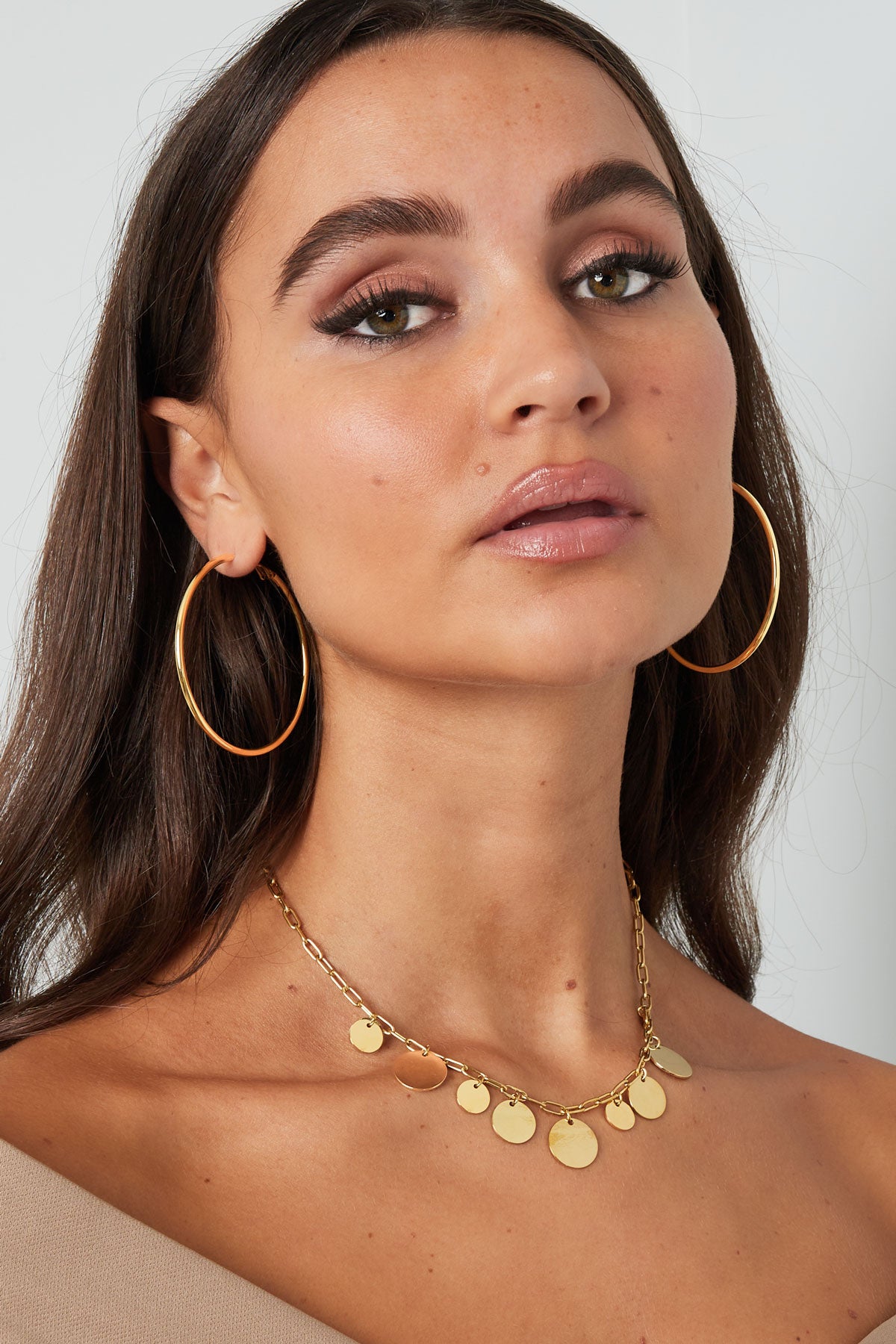 Close profile shot of a woman with sleek gold hoop earrings and a gold necklace with coin charms