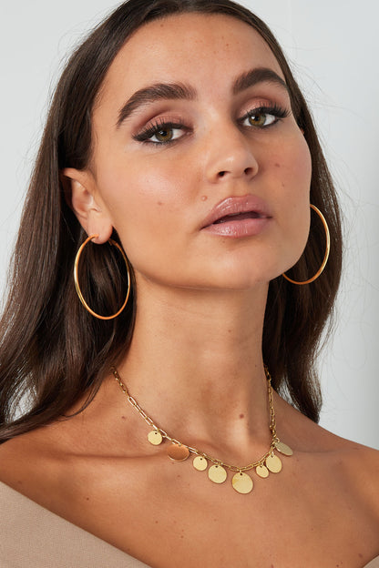 Close profile shot of a woman with sleek gold hoop earrings and a gold necklace with coin charms