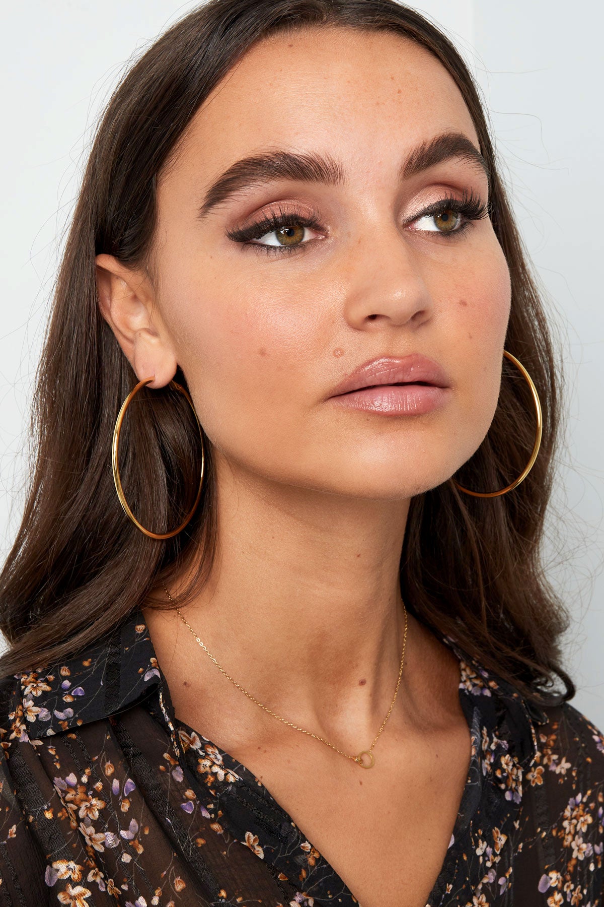 Close-up of model wearing glossy gold hoop earrings highlighting the minimalist design