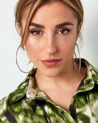 A woman wearing large, thin silver hoop earrings and a green patterned shirt.