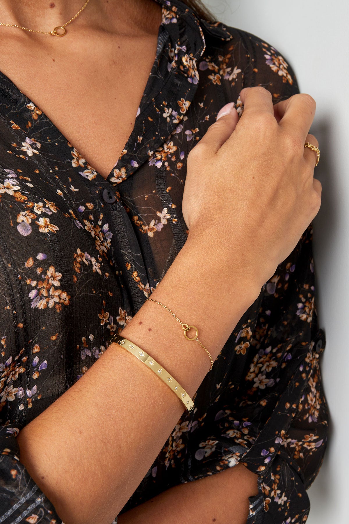Close-up of a woman wearing the gold linked circle bracelet alongside a decorative gold bangle, dressed in a black floral blouse