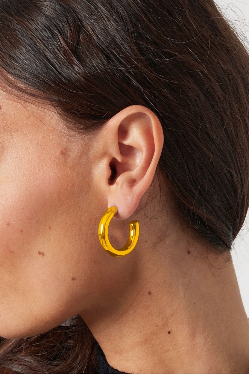 A person wears Big Mood Hoops: thick, polished gold chunky circular earrings in a minimal, modern style.