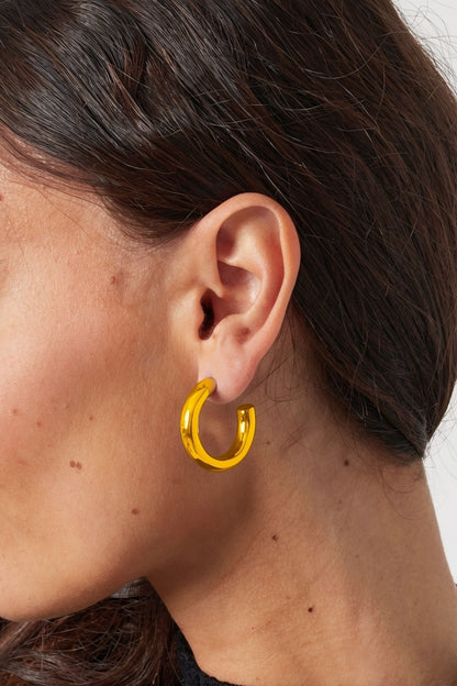 A person wears Big Mood Hoops: thick, polished gold chunky circular earrings in a minimal, modern style.