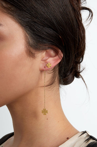 Close-up of woman wearing one gold-tone four leaf clover stud earring paired with a long chain drop earring