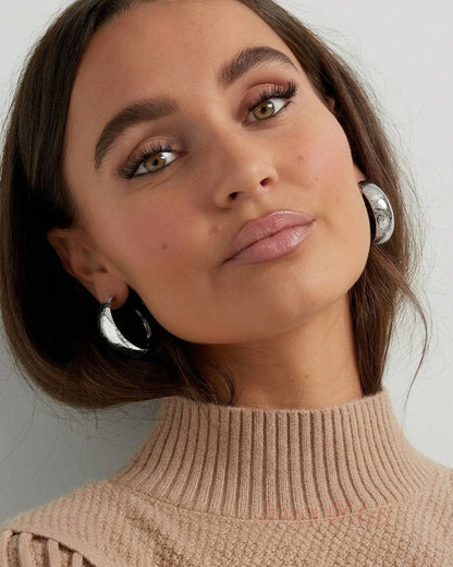 Thick, silver-finished hammered hoop earrings worn on earlobes.