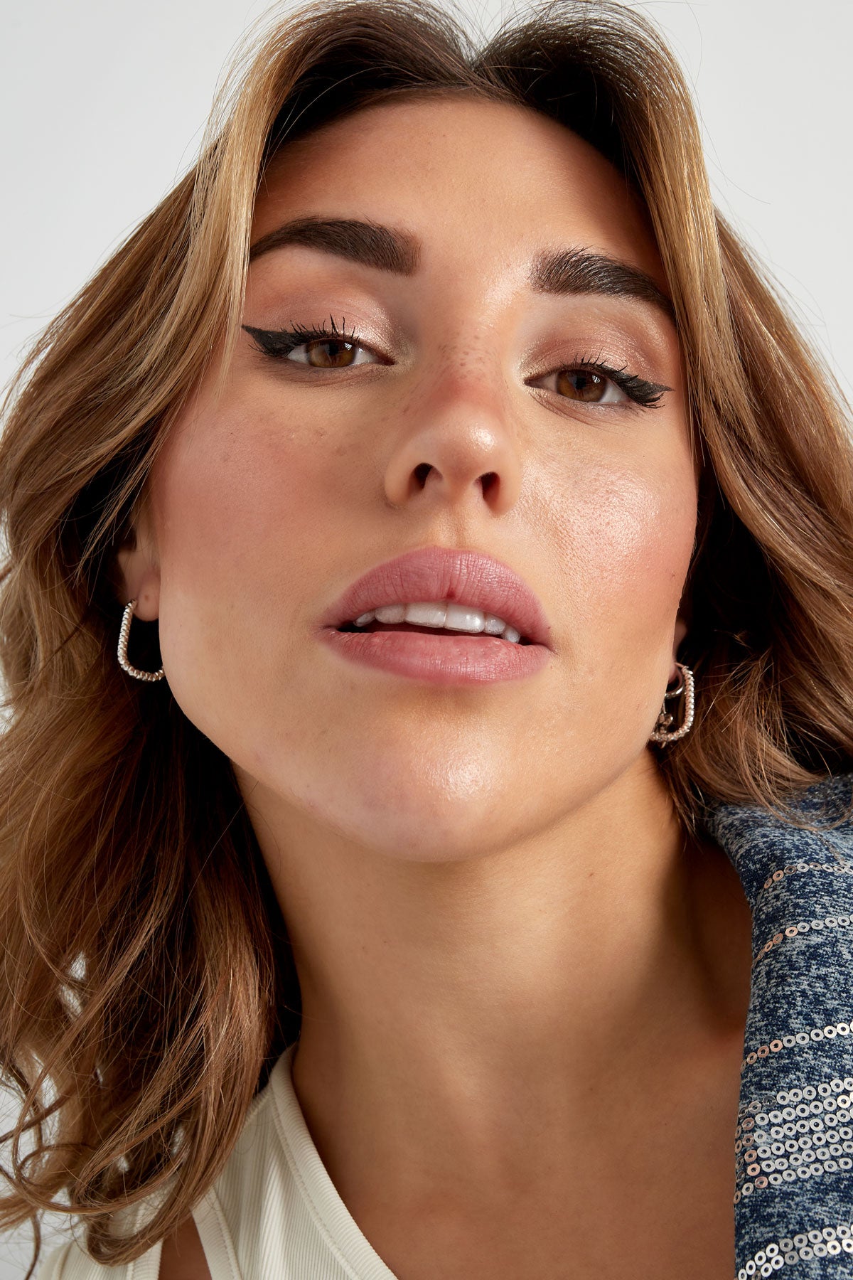 Close-up of model wearing silver textured oval hoop earrings with natural makeup