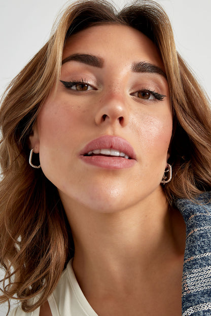 Close-up of model wearing silver textured oval hoop earrings with natural makeup