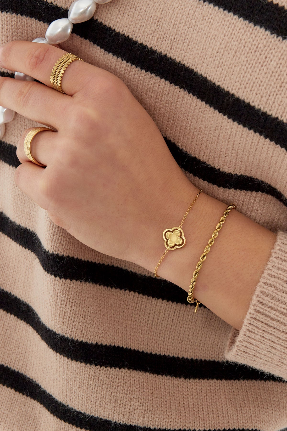 Model wearing gold double clover charm bracelet and matching gold rings on hand with striped sweater background