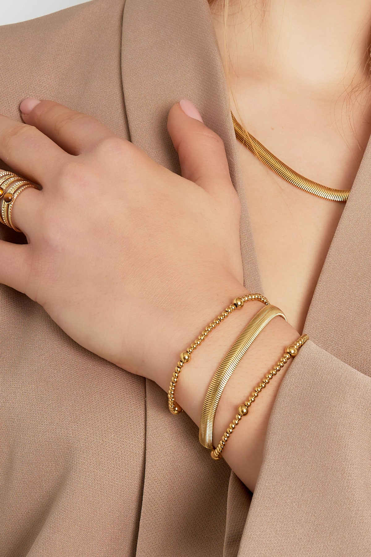 Close-up of woman’s wrist wearing layered gold chain and bead bracelets