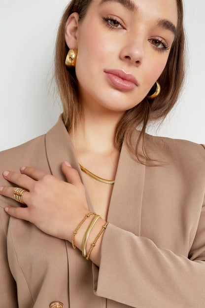 Woman showcasing gold chain bracelet along with matching ring and earrings in beige blazer