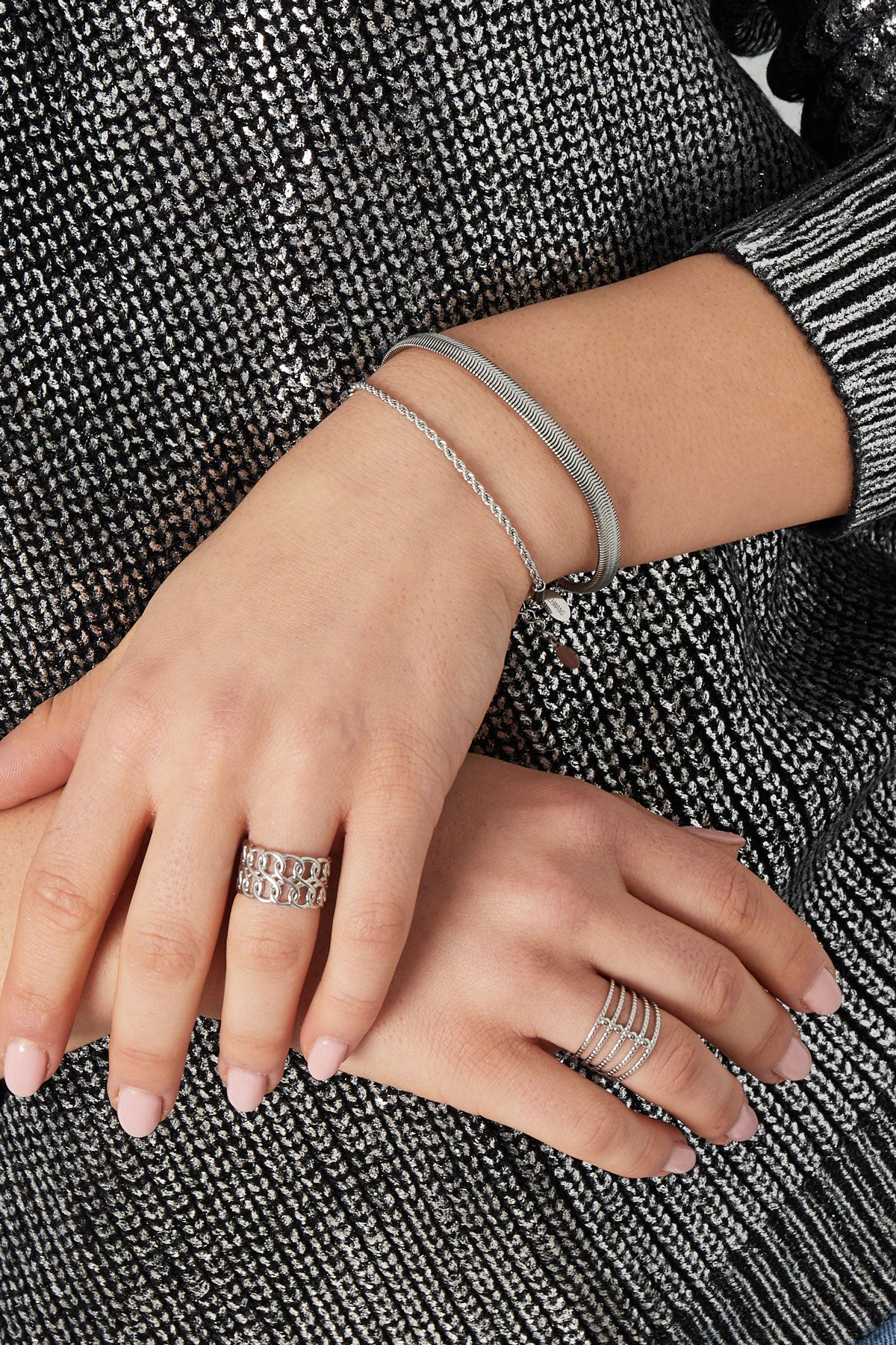 Close-up of silver chain bracelet and rings on woman’s hand with a silver textured top
