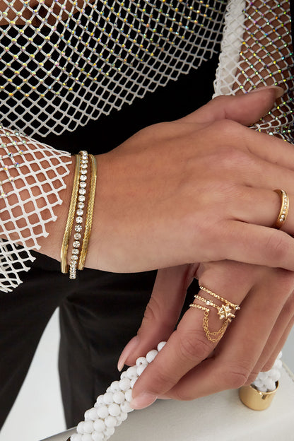 Gold layered chain bracelet with rhinestones worn on wrist paired with delicate gold rings and white beaded bag