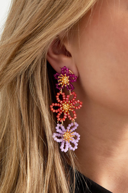 Close-up of floral beaded dangle earring worn on ear showing purple, orange and lavender flowers
