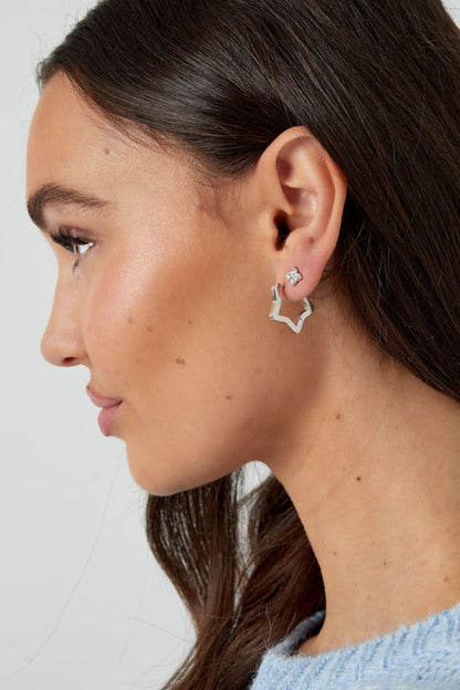 Profile view of woman wearing silver-tone four-stone stud earrings paired with star-shaped hoop earrings