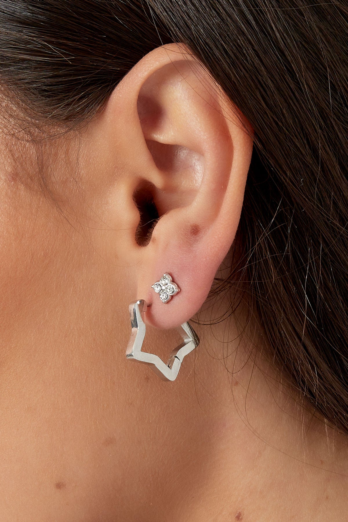 Close-up profile of woman's ear showing silver-tone four-stone stud earring with star-shaped hoop earring