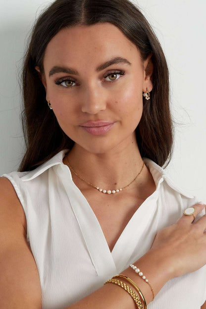 Close-up of a woman's wrist adorned with the gold chain pearl bracelet alongside other gold bracelets