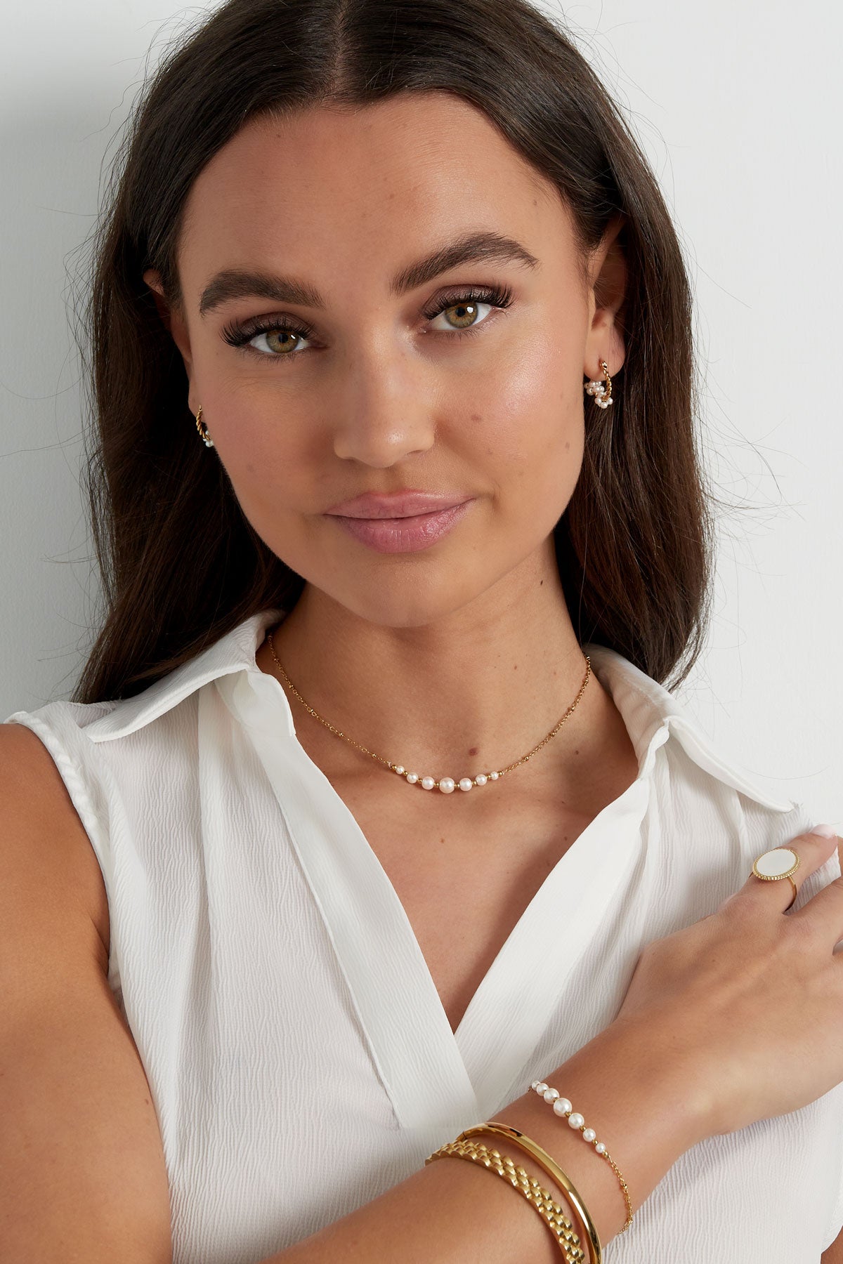 Close-up of a woman's wrist adorned with the gold chain pearl bracelet alongside other gold bracelets
