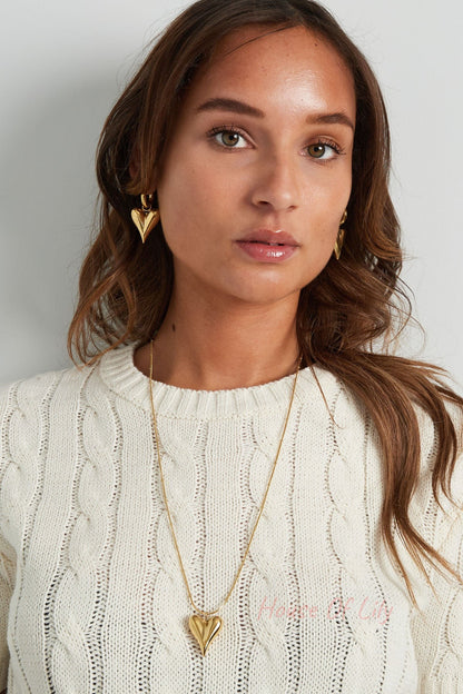 Woman wearing gold chunky heart hoop earrings paired with a gold heart pendant necklace and cream cable knit sweater