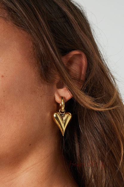 Close up of woman wearing gold chunky heart hoop earrings with loose brown hair