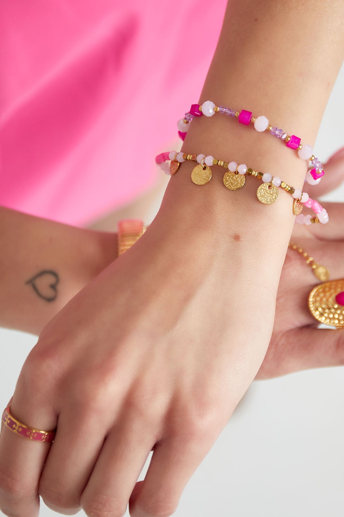 Two vibrant beaded bracelets on a woman's wrist wearing a bright pink outfit, featuring pink beads and gold disc charms