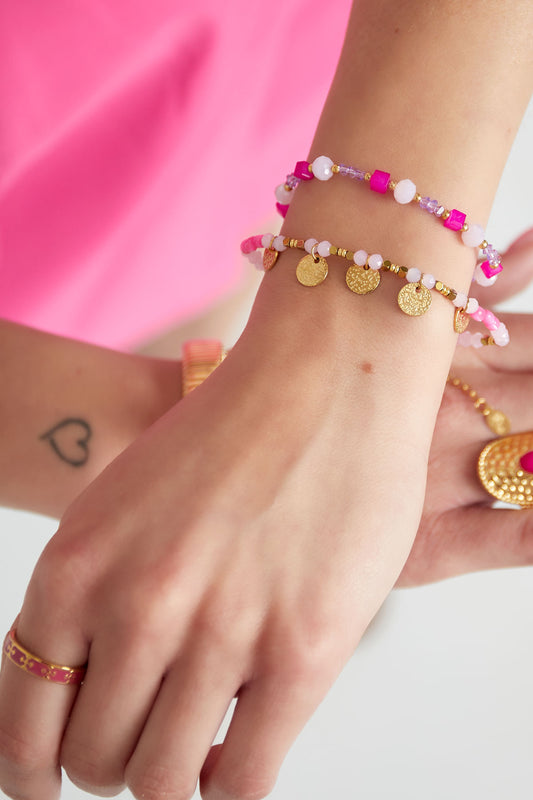 Two vibrant beaded bracelets on a woman's wrist wearing a bright pink outfit, featuring pink beads and gold disc charms